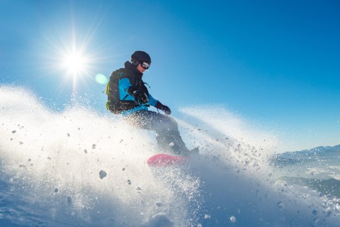 Snowboarder Riding Red Snowboard in the Mountains at Sunny Day. Snowboarding and Winter Sports